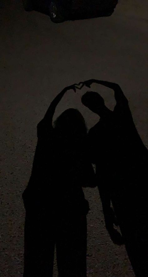 two people standing in the dark with their arms around each other and one person reaching up