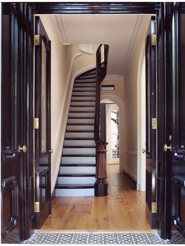 an entry way leading to a staircase with wooden floors and black painted doors on either side