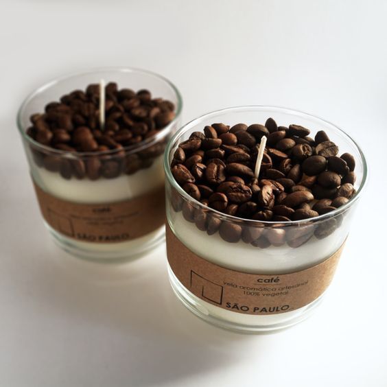 two candles with coffee beans in them on a white surface, next to each other