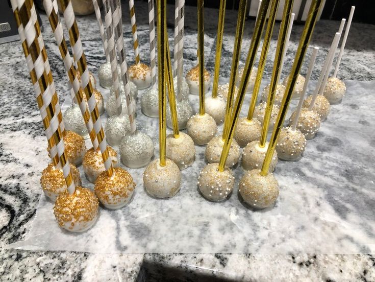 there are many gold and white candy balls on the table with striped paper straws