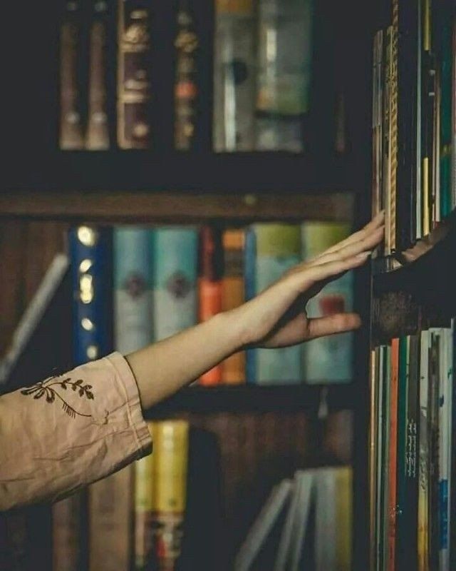 a person reaching out from behind a book shelf in front of bookshelves with their hands