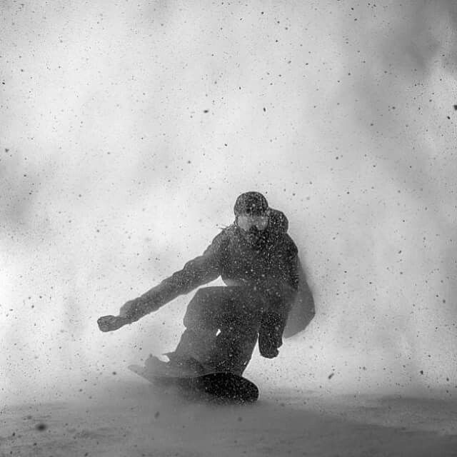 a man riding a snowboard down the side of a snow covered slope on a snowy day