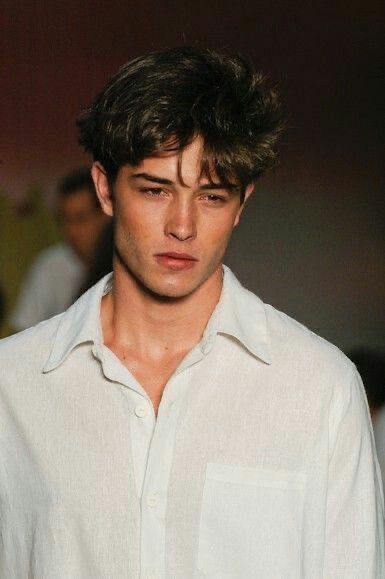 a young man in a white shirt is looking at the camera while he walks down the runway