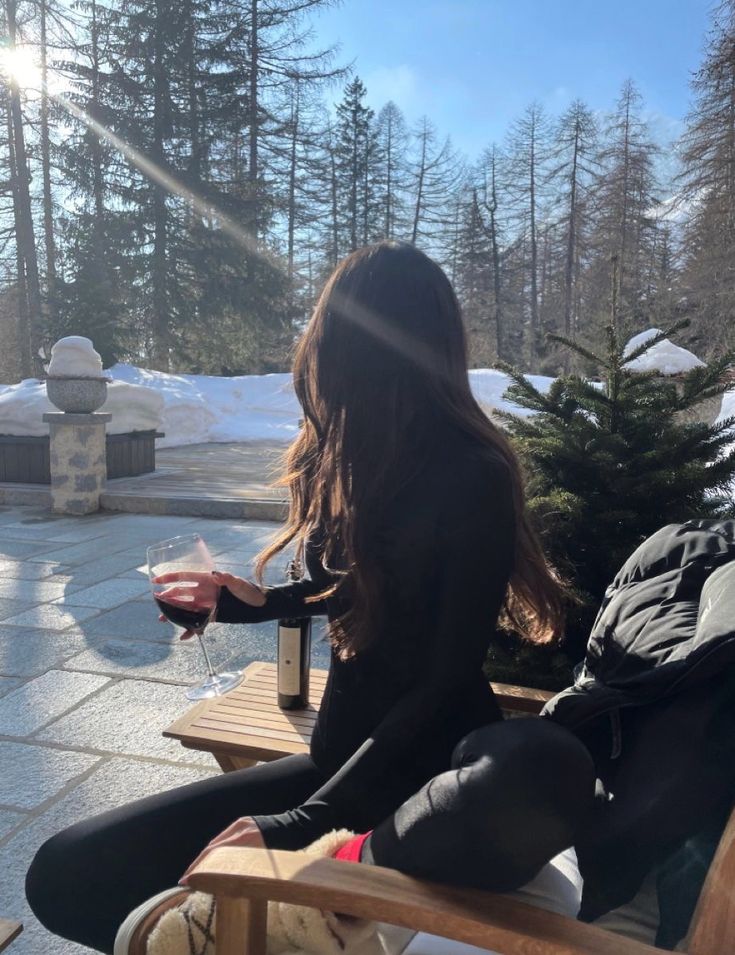 a woman sitting on top of a wooden bench holding a glass of wine in her hand