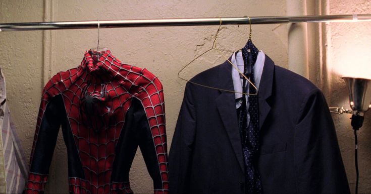 two suits are hanging on a clothes rack in front of a wall with a lamp