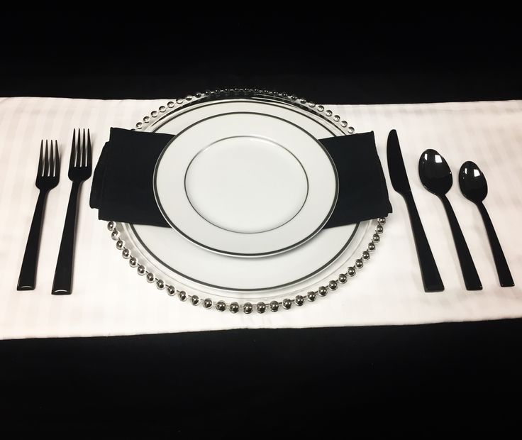 a white plate topped with silverware next to a black and white place setting on a table