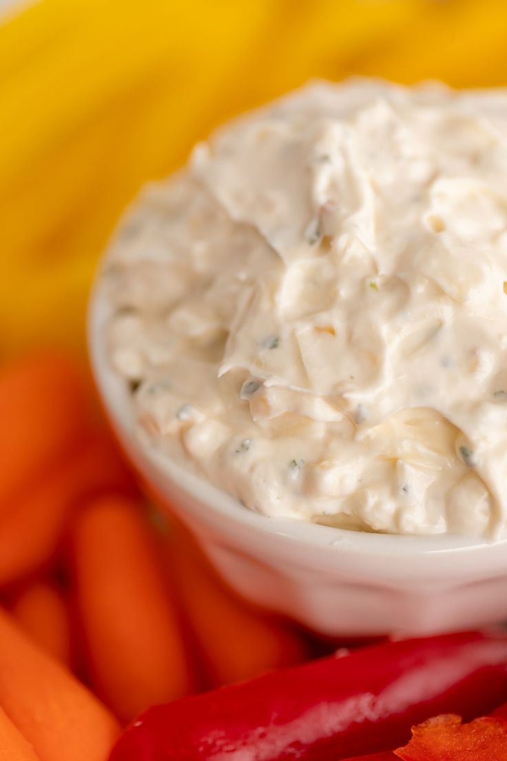 a white bowl filled with dip surrounded by carrots and peppers