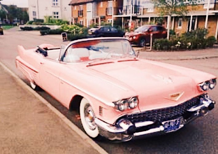 an old pink car is parked on the side of the road