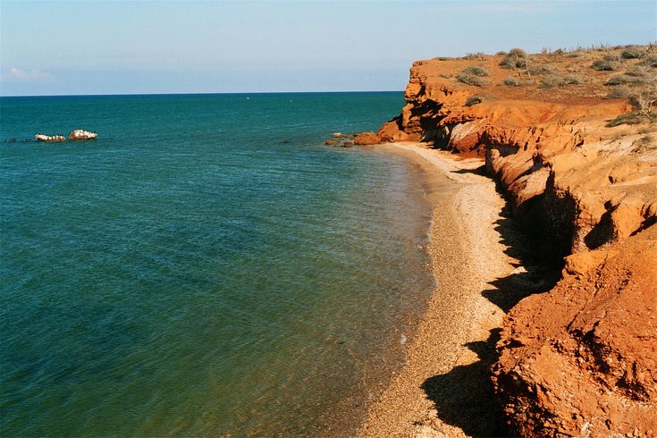 there is a boat that is in the water at the beach near some rocks and sand