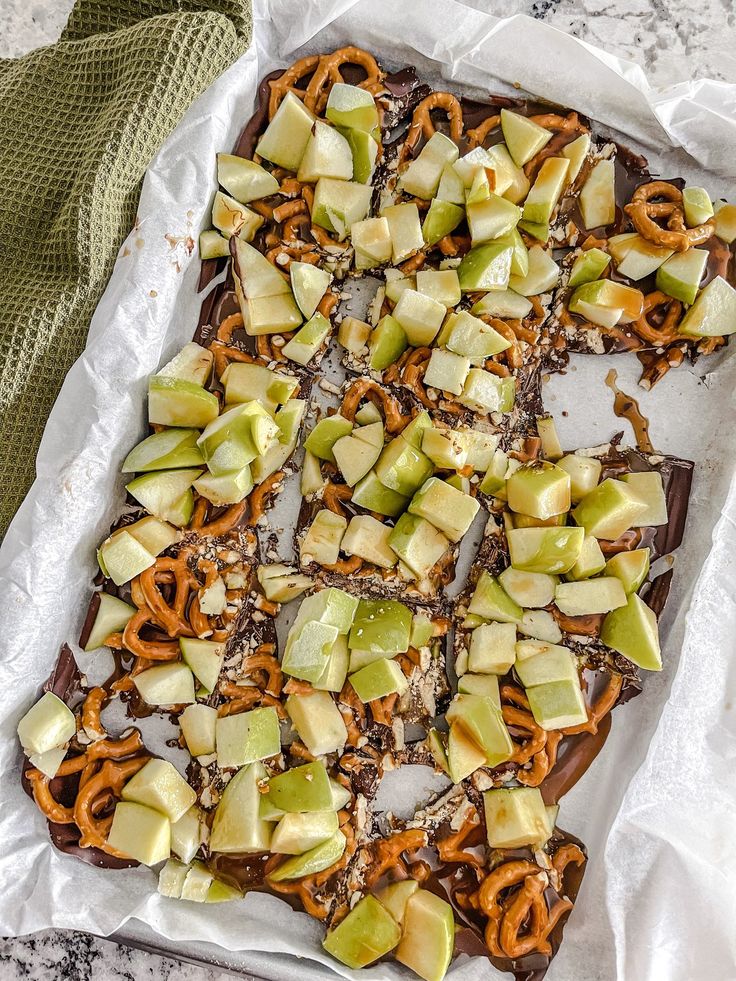 an apple and pretzel snack on a sheet of wax paper with some pretzels cut into squares