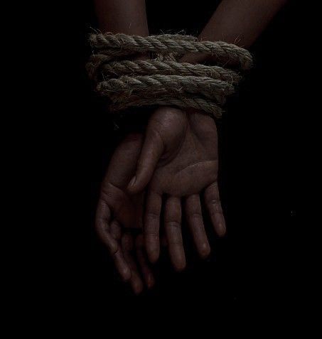 two hands tied up with rope in the dark, on top of eachother