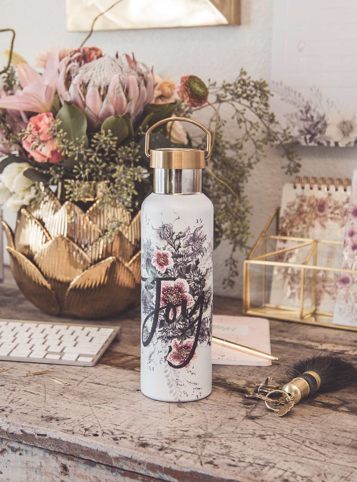 a white bottle sitting on top of a wooden table next to a keyboard and flowers