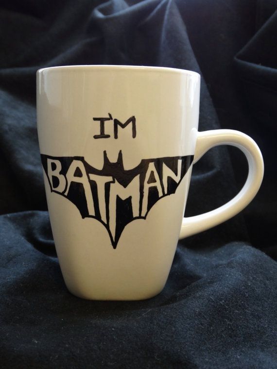 a white coffee cup with the words i'm batman printed on it, sitting on a black cloth