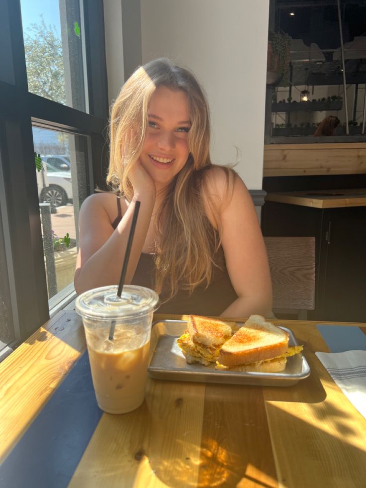 a woman sitting at a table with a sandwich and drink