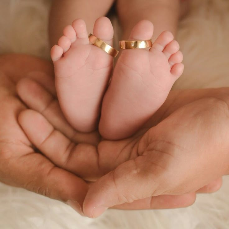 a person holding a baby's feet in the palm of their hand, with two gold rings on it