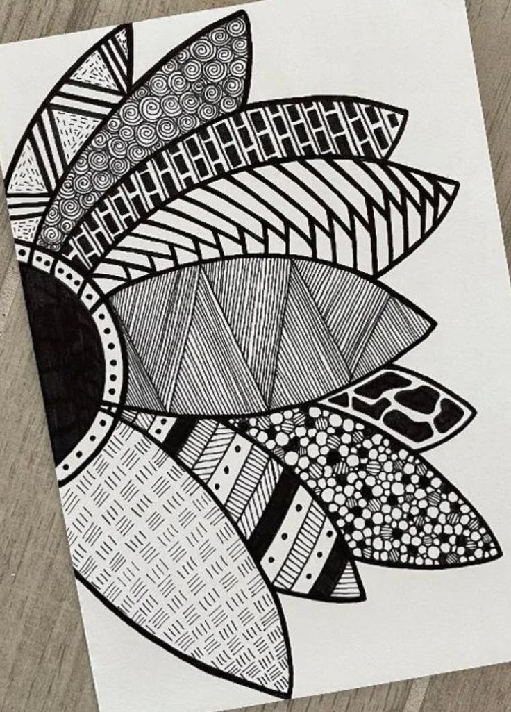 a black and white drawing on paper with an abstract design in the middle, sitting on a wooden surface