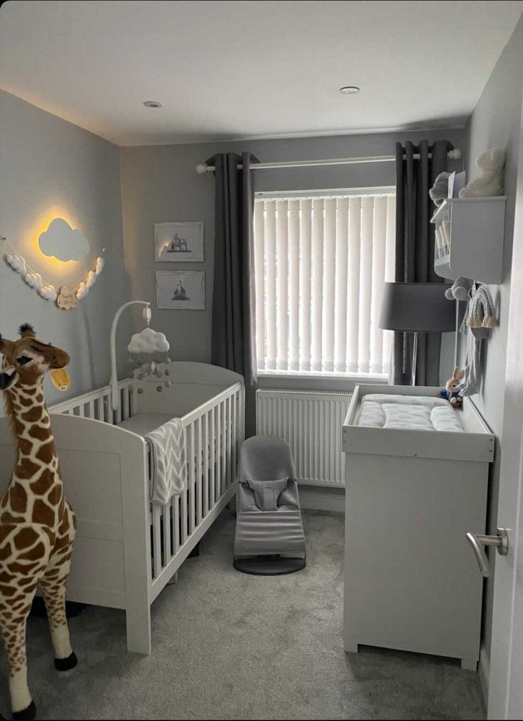 a giraffe standing next to a baby crib in a room with grey walls