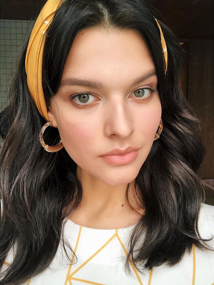 a woman with long black hair wearing a yellow headband and hoop earrings