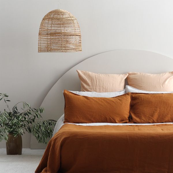 a bed with orange sheets and pillows next to a potted plant