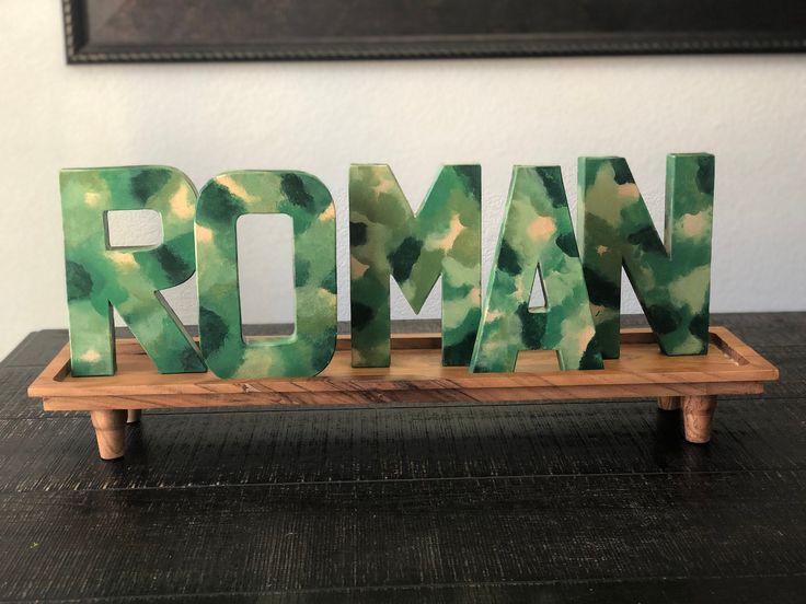 the word roman spelled with green paint on a wooden stand in front of a painting