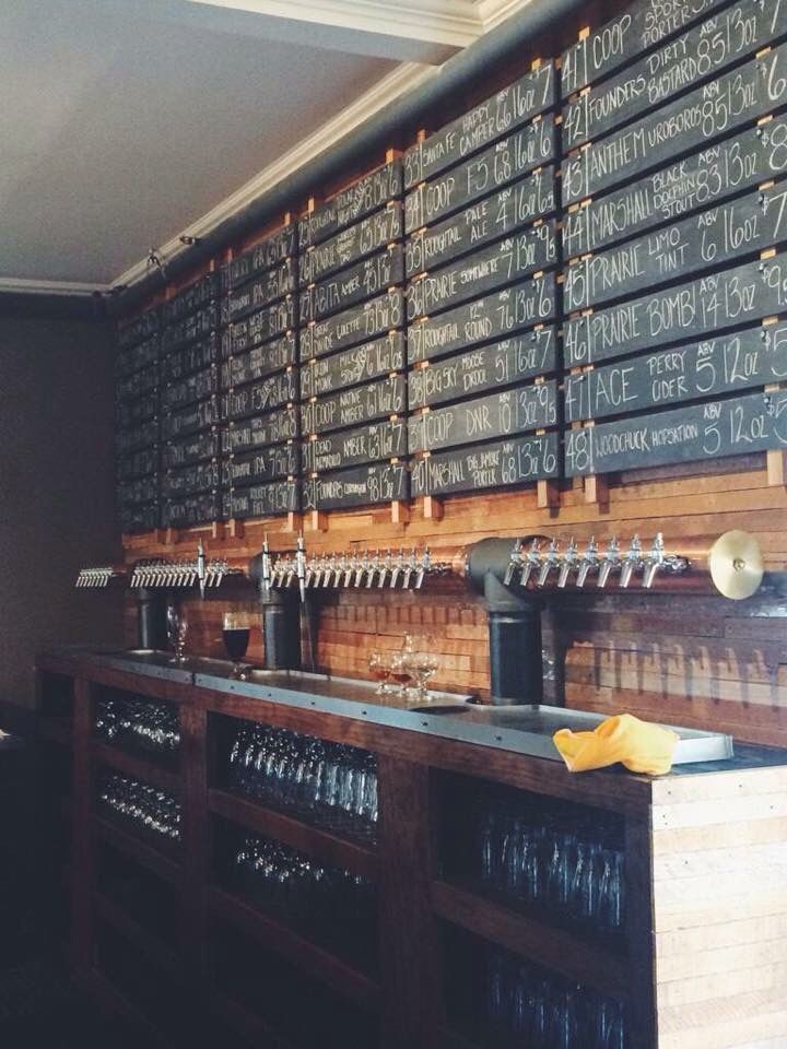 a long row of beer taps in front of a wall with chalk writing on it