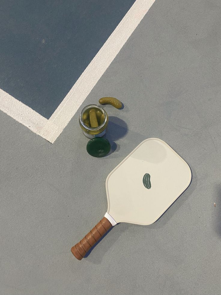 a tennis racquet laying on the ground next to a bowl of pickles