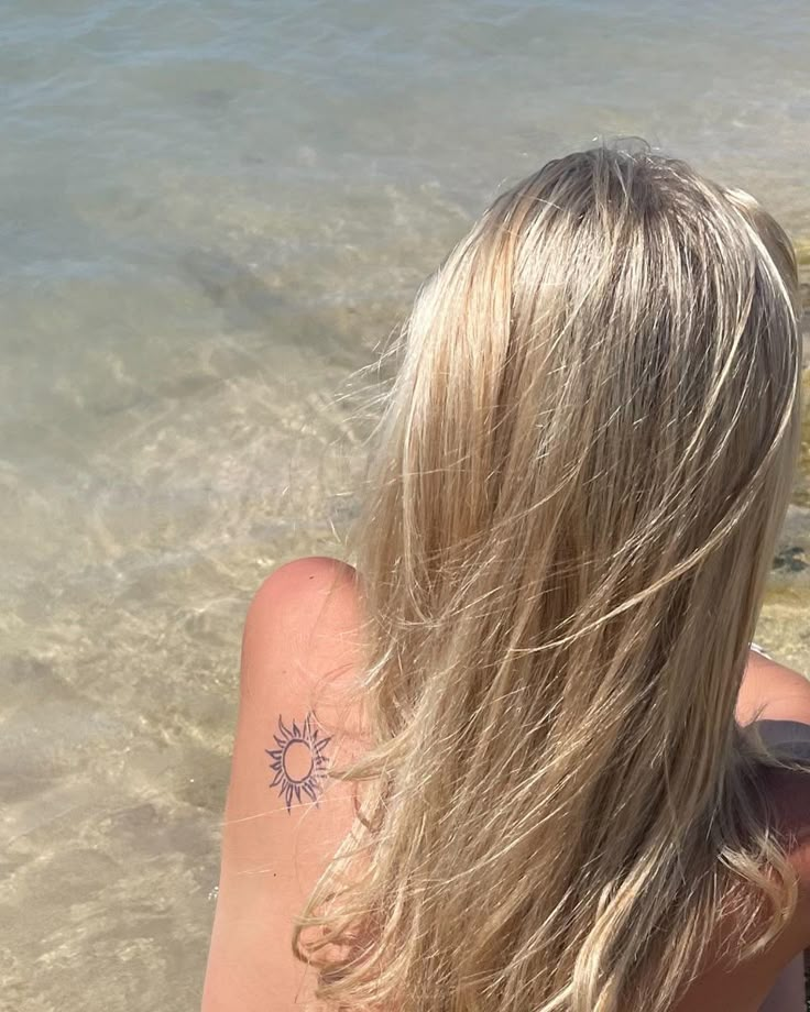 the back of a woman's head with a sun tattoo on her left shoulder