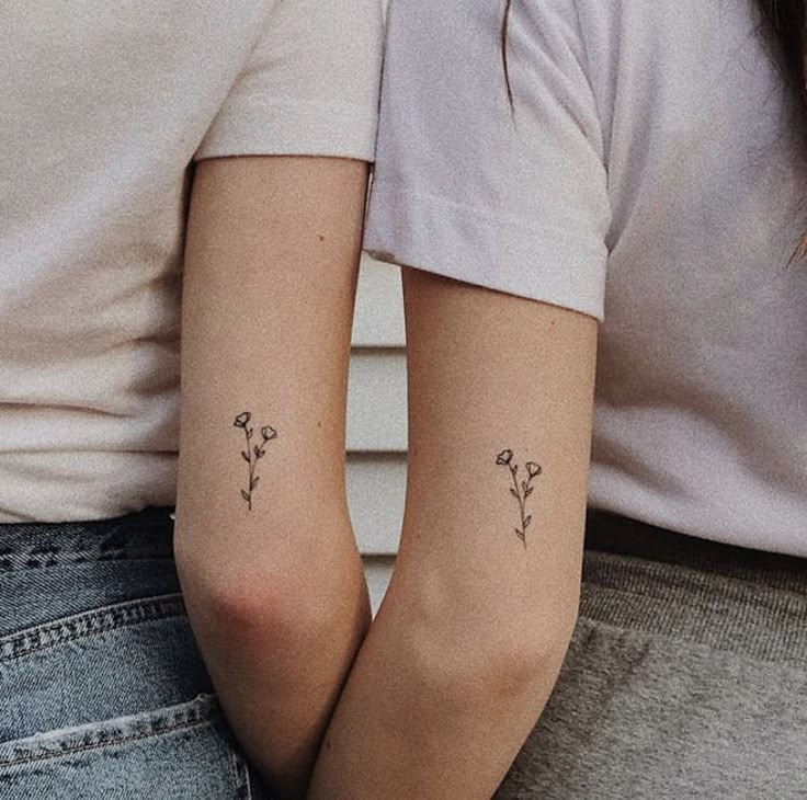 two women with matching tattoos on their arms, one holding the other's arm