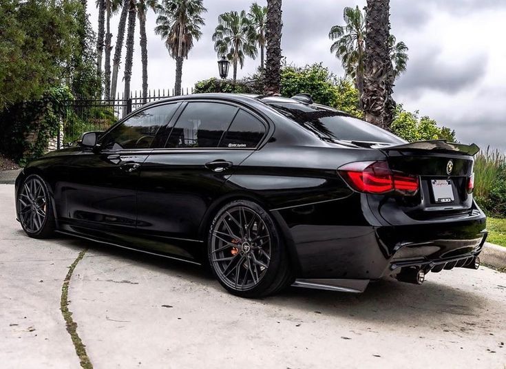 a black car parked on the side of a road with palm trees in the background