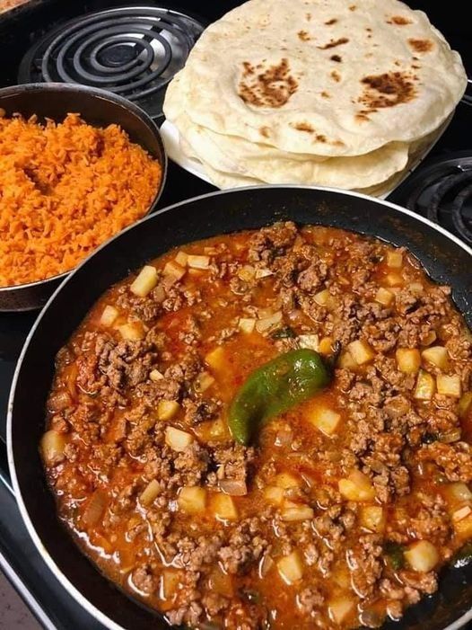 a pan filled with food next to two bowls of rice and tortilla bread