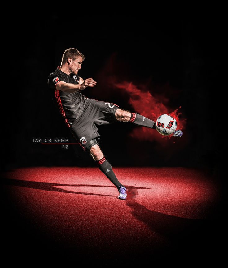 a man kicking a soccer ball on top of a red floor in front of a black background