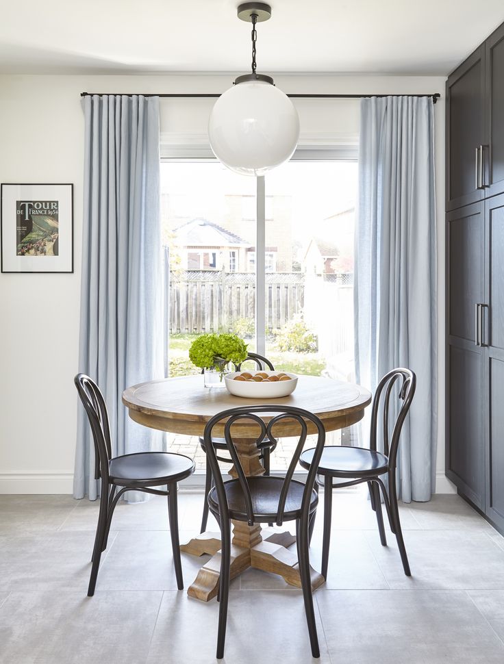 a dining room table with four chairs and a vase on top of it in front of a window