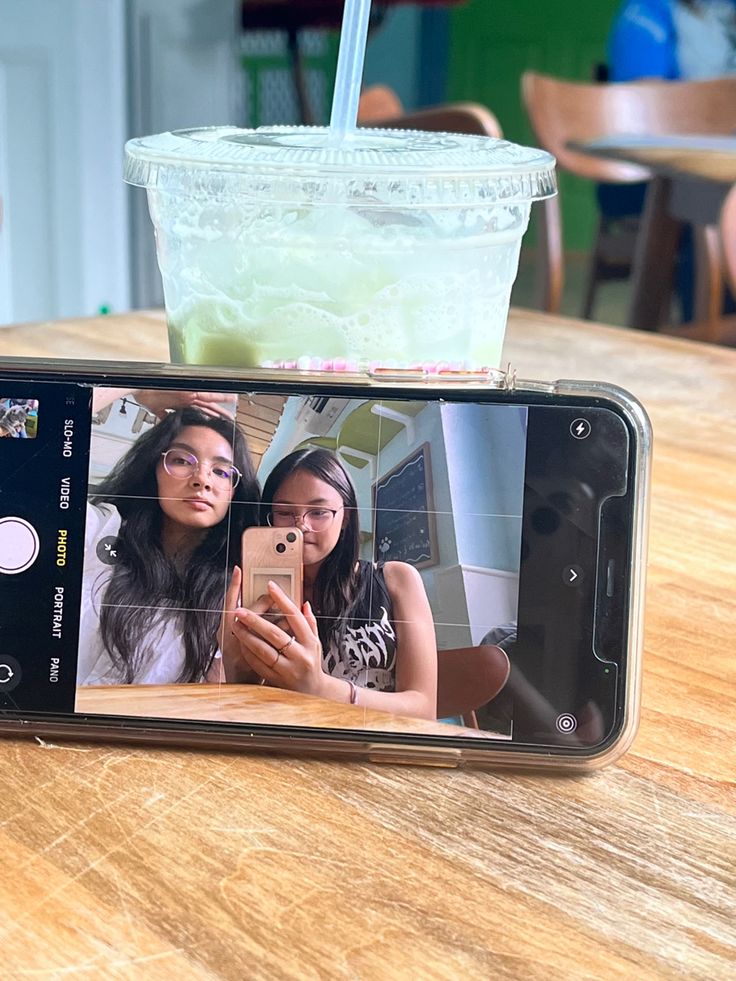 a cell phone sitting on top of a wooden table next to a cup of drink