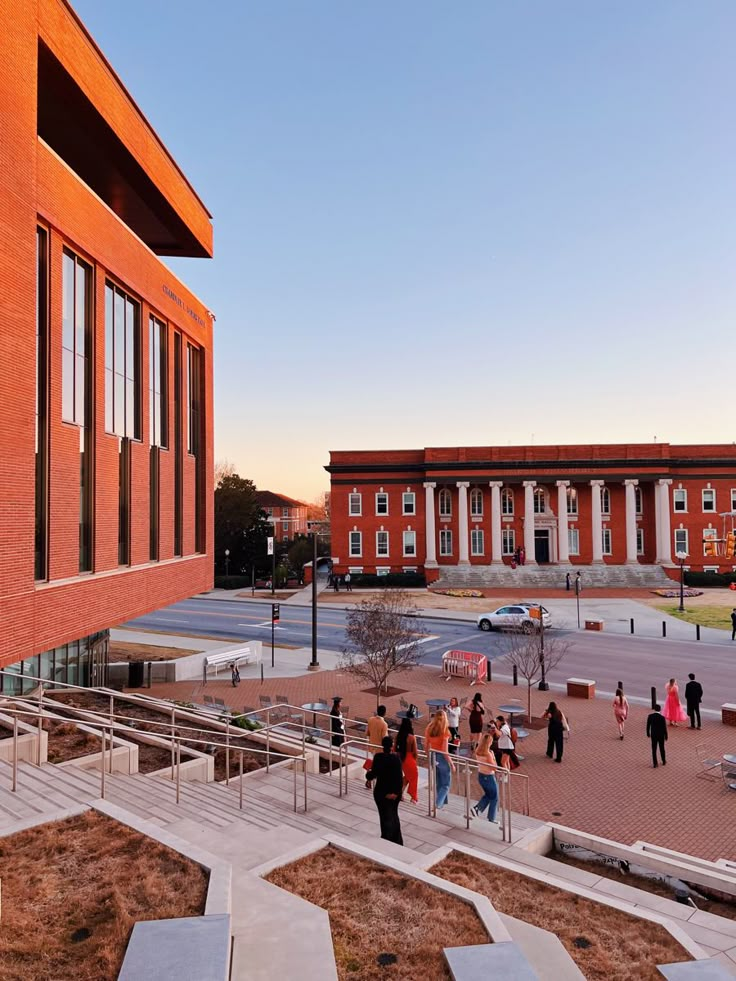 many people are walking around in front of an orange brick building with stairs leading up to it