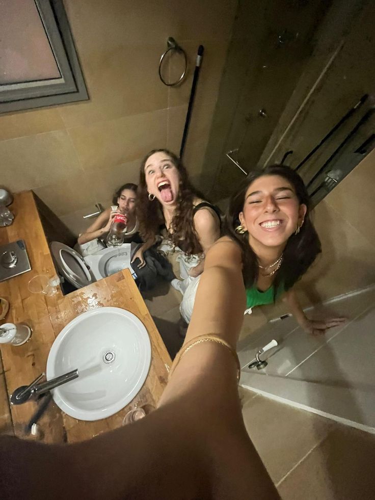 three women are taking a selfie in the mirror while sitting at a bathroom sink