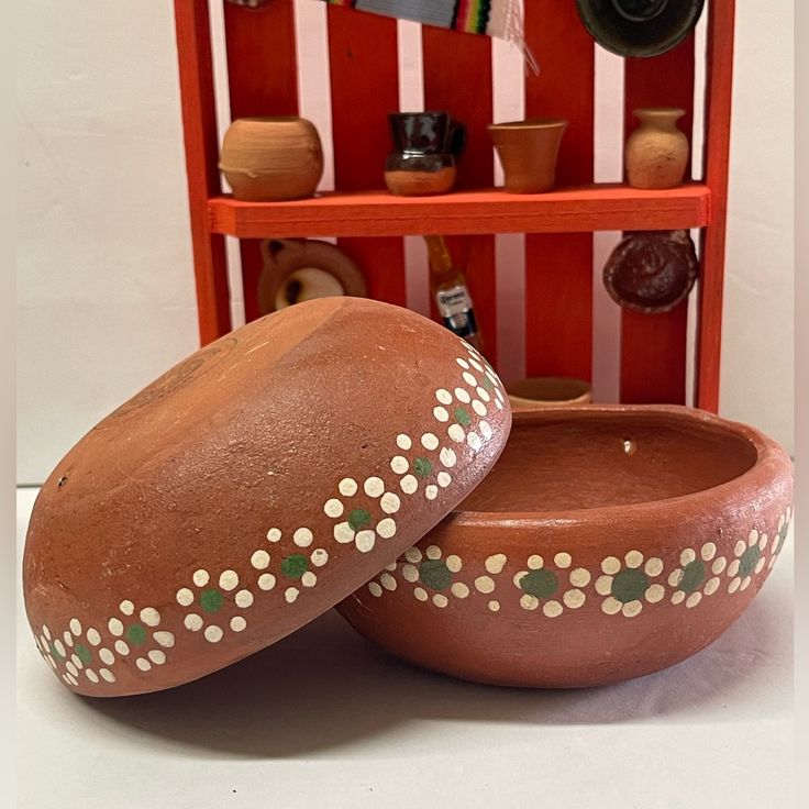 two clay bowls sitting on top of a table next to a shelf filled with pots