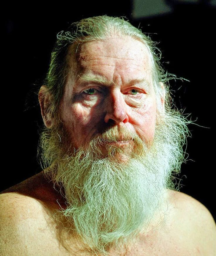 an old man with a long beard and no shirt is looking at the camera while he stares into the distance