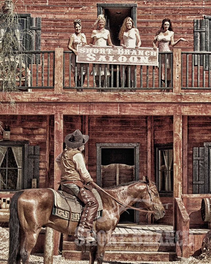 a man riding on the back of a brown horse next to a tall wooden building