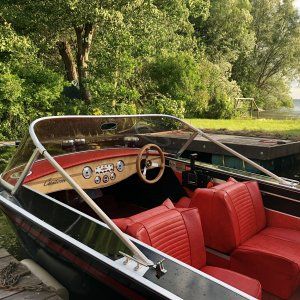 a red and black boat sitting next to a body of water with trees in the background