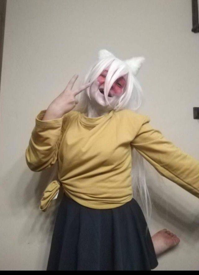 a woman in a yellow shirt and black skirt with white hair wearing a cat mask