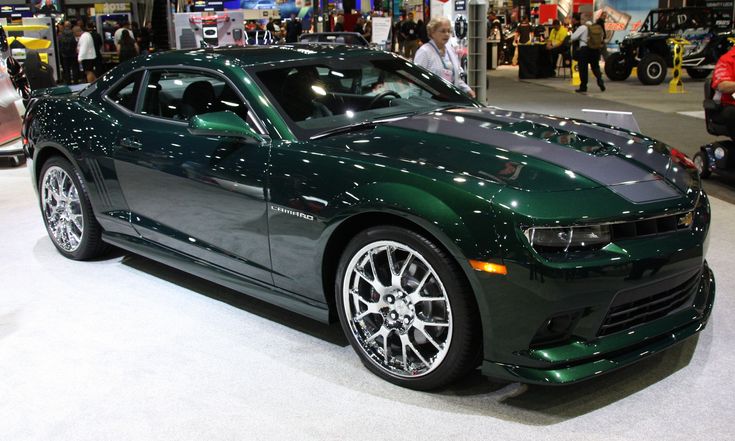 a green chevrolet camaro is on display at an auto show with people looking around