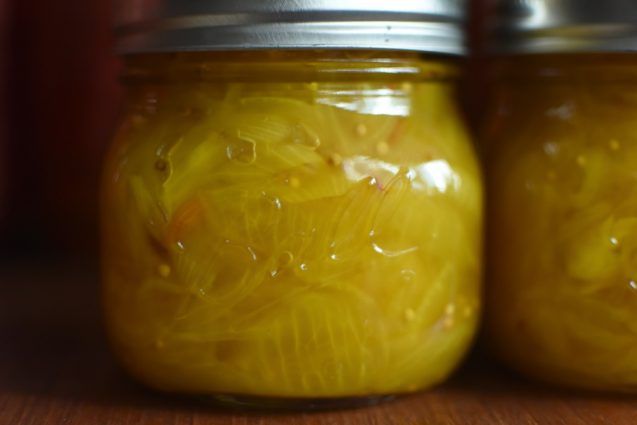 two jars filled with pickles sitting on top of a wooden table