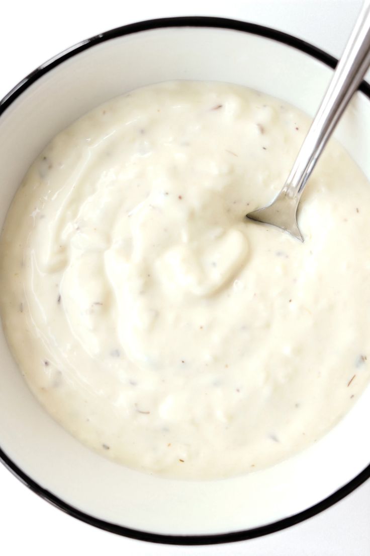 a white bowl filled with cream sauce on top of a table next to a spoon