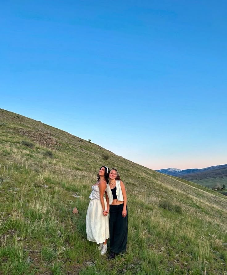 two women standing in the grass on top of a hill