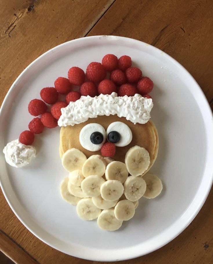 a white plate topped with pancakes covered in fruit and a face made out of bananas