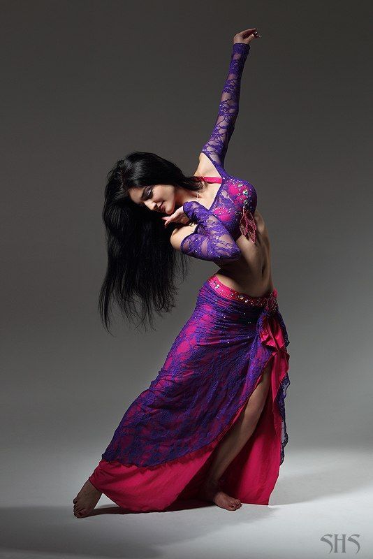 a woman in a purple and pink dress is dancing with her arms out to the side