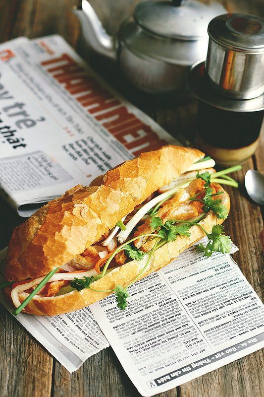 a sandwich sitting on top of a newspaper next to a tea pot and cup filled with liquid