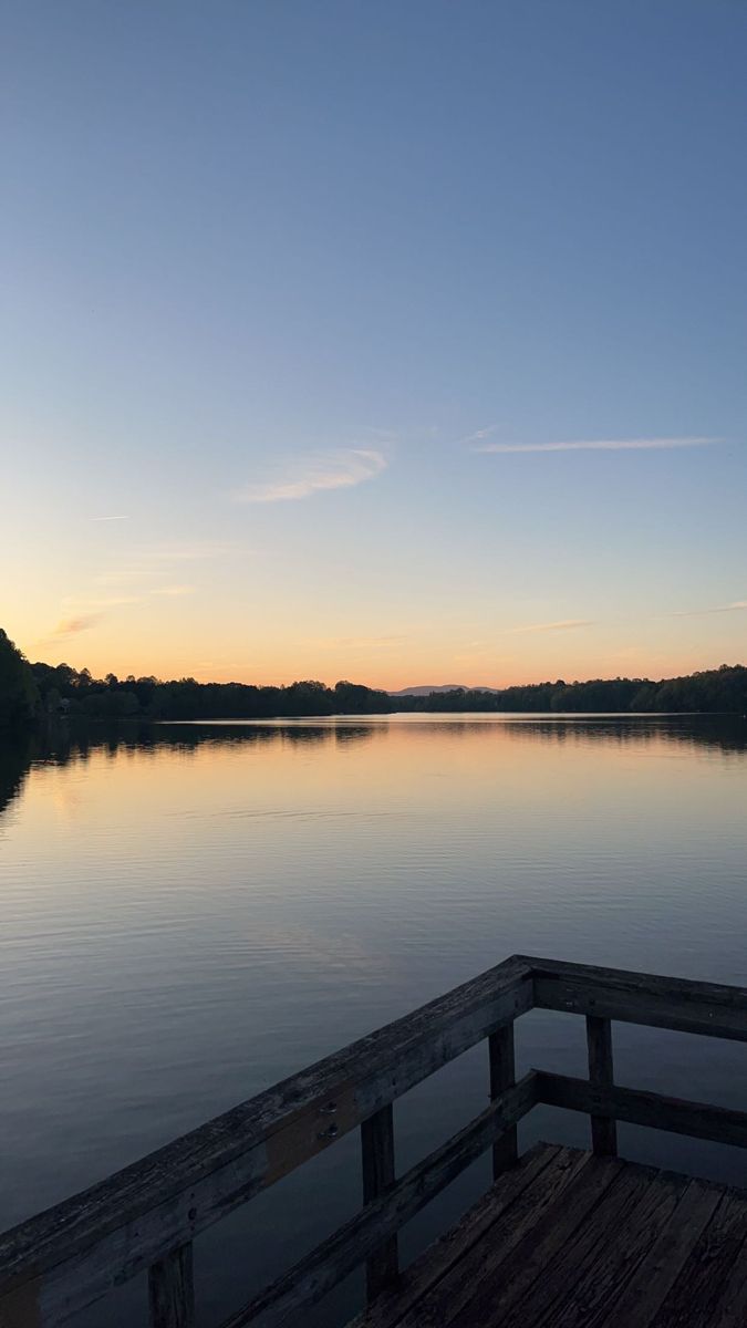 a wooden dock sitting on top of a lake next to a lush green forest under a blue sky