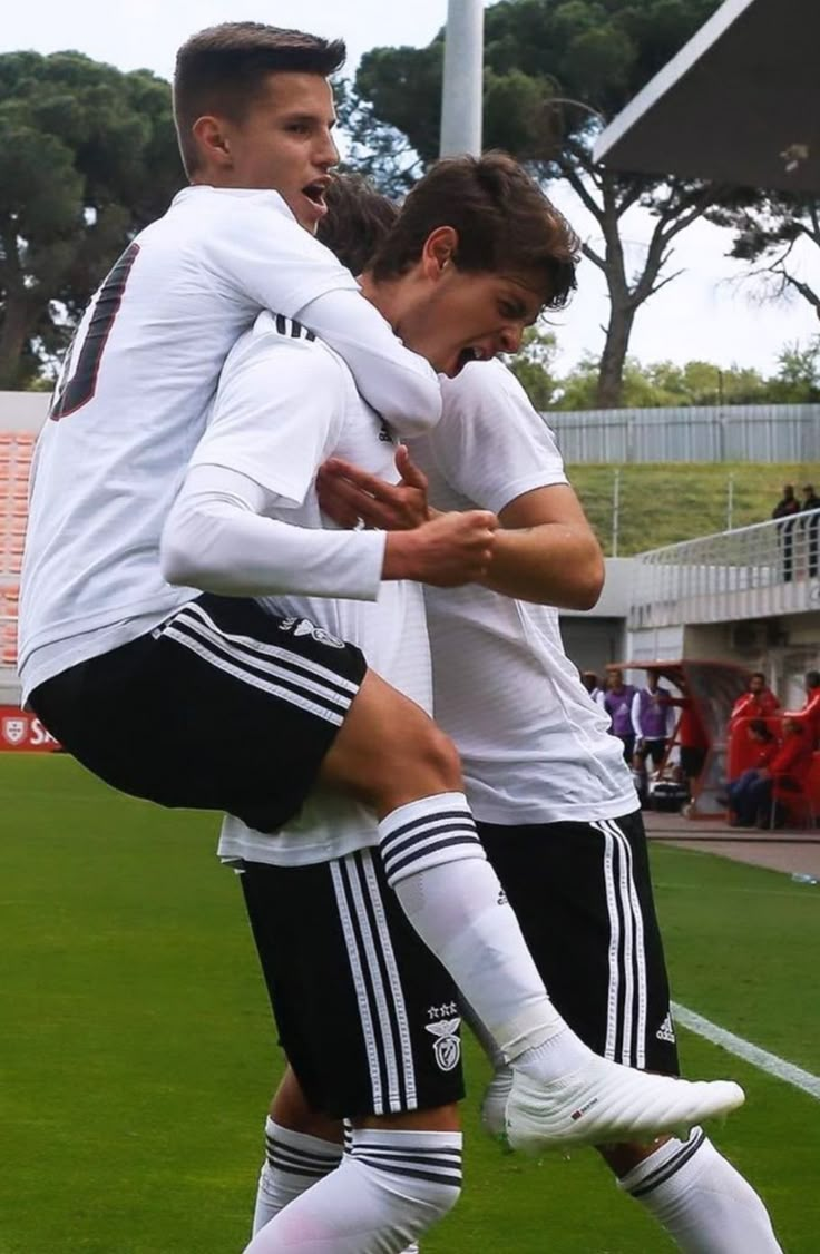 two young men are playing soccer on the field with their arms around each other as they hug