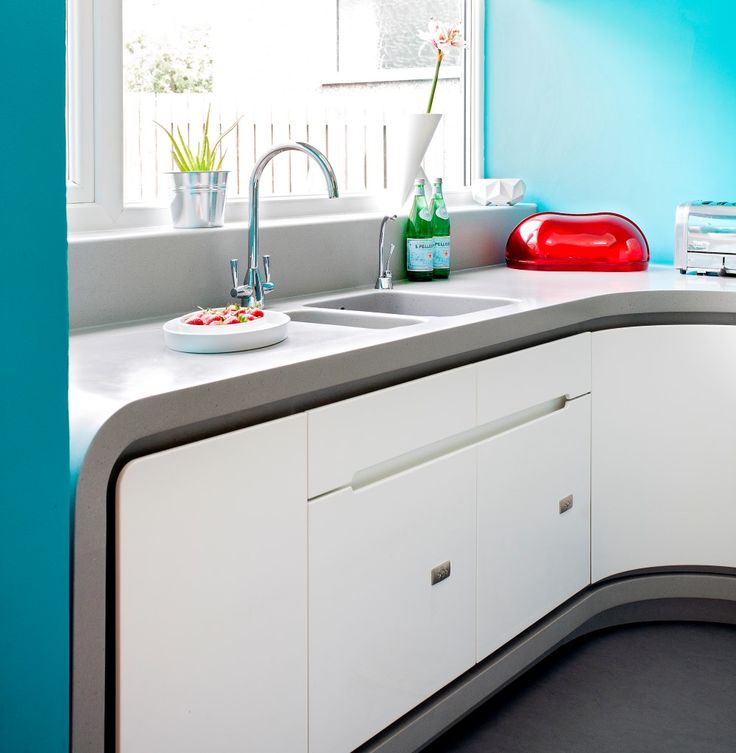 a kitchen with blue walls and white counter tops, including a bowl of fruit on the sink